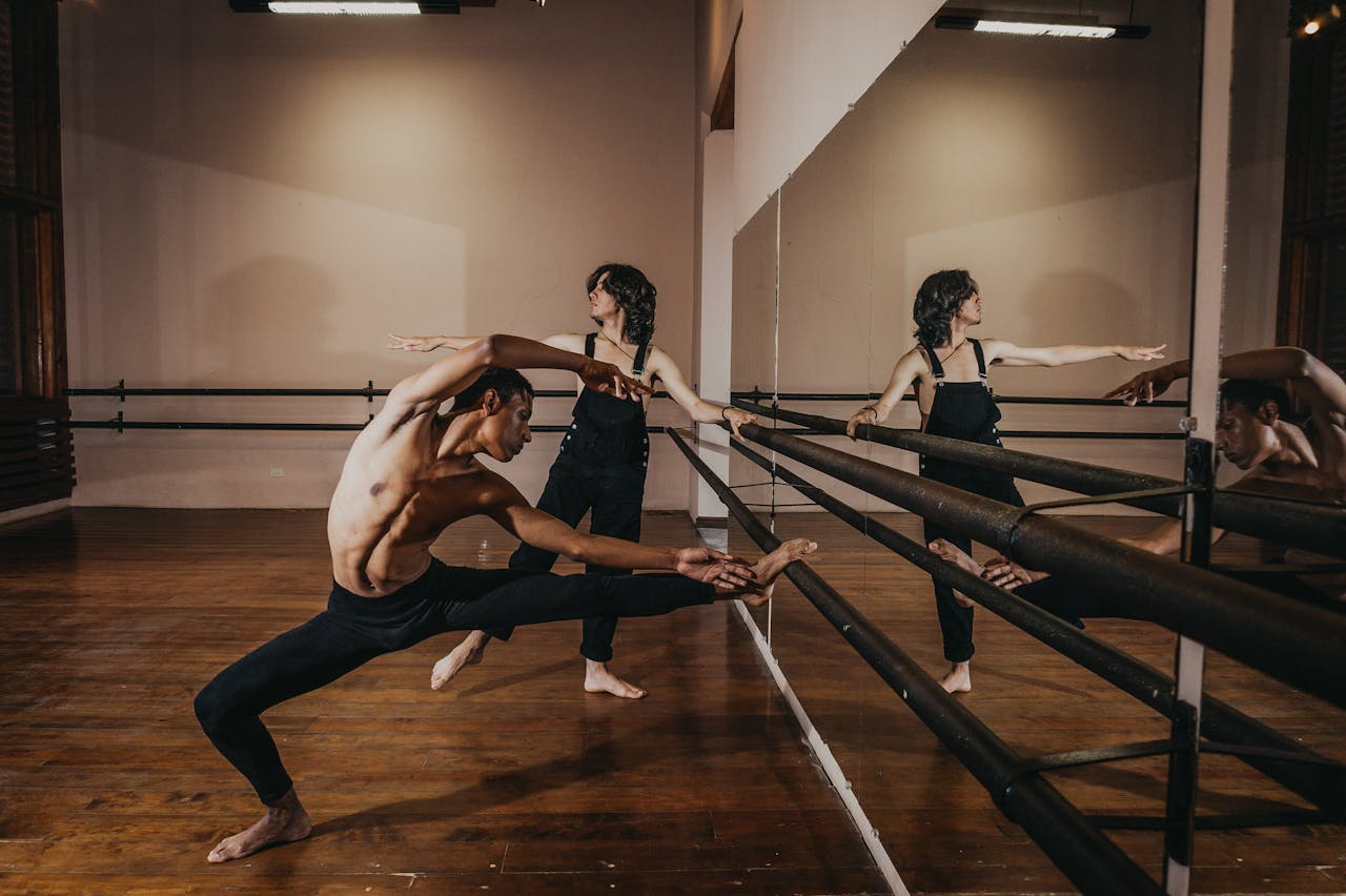 Two ballet dancers perform flexible poses during rehearsal in a dance studio.